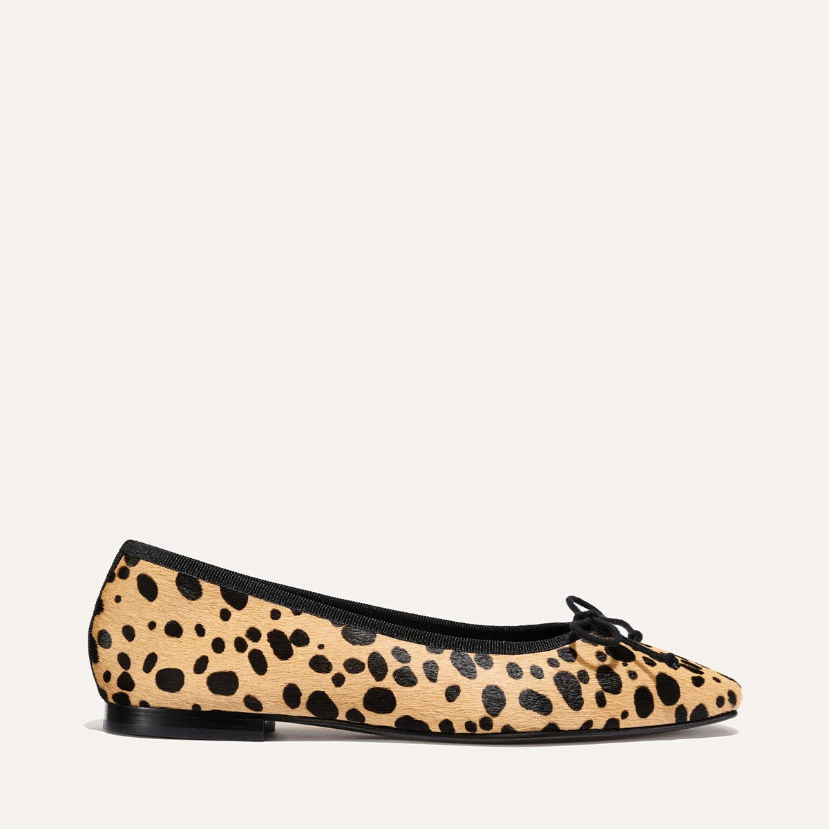 The Fonteyn by Margaux: a tan cheetah haircalf ballet flat featuring a rounded toe, sleek black trim, and a petite bow on top, crafted for all-day comfort with its flat black sole—photographed against a plain light background.