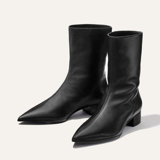 The Hayes Boot - Black Nappa by Margaux, a pair of black mid-calf leather boots featuring pointed toes and low block heels, is displayed on a light background.