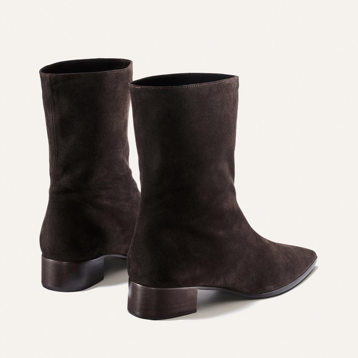 A pair of The Hayes Boot by Margaux in dark chocolate suede, featuring low chunky heels and pointed toes, is shown from the back and side against a plain light background.