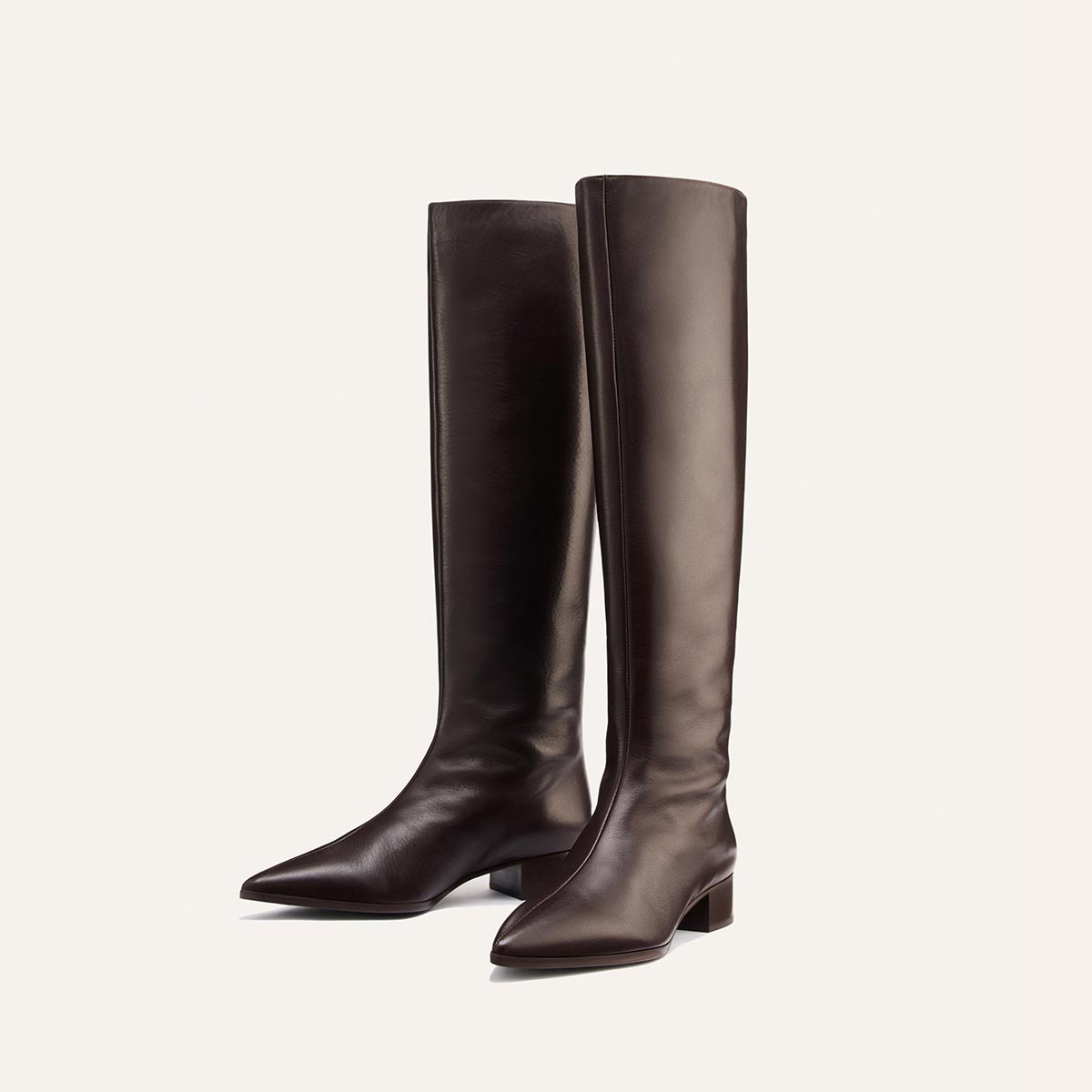 A pair of sleek, dark chocolate leather Margaux Hayes Knee-High Boots with pointed toes and low block heels, crafted for comfort and standing upright on a light background.