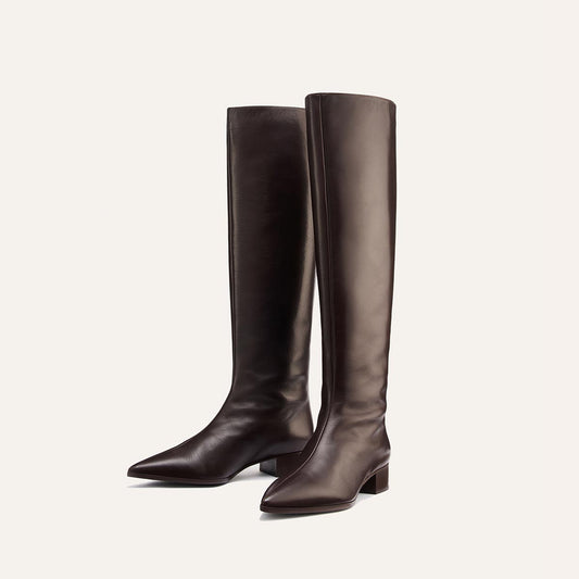 A pair of sleek, dark chocolate leather Margaux Hayes Knee-High Boots with pointed toes and low block heels, crafted for comfort and standing upright on a light background.