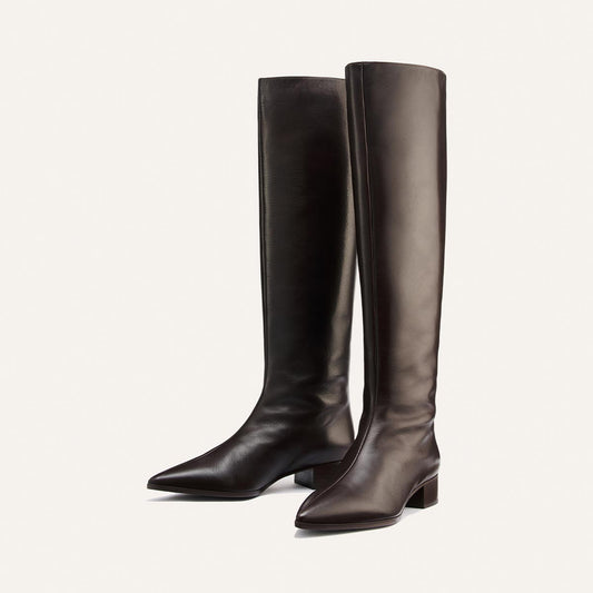 A pair of handmade tall boots crafted from soft dark chocolate calf leather, the Hayes Knee-High Boot by Margaux features pointed toes and low block heels for comfort, displayed against a plain white background.