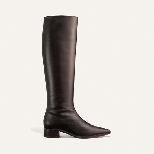 The Hayes Knee-High Boot in Dark Chocolate Calf by Margaux is a handmade tall boot crafted from soft leather, featuring a knee-high silhouette with a low block heel, almond toe, and smooth finish. Shown against a light background, it offers a comfortable yet sophisticated look.