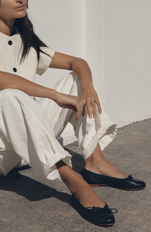 Person wearing navy flats sitting on a concrete surface with a white wall in the background