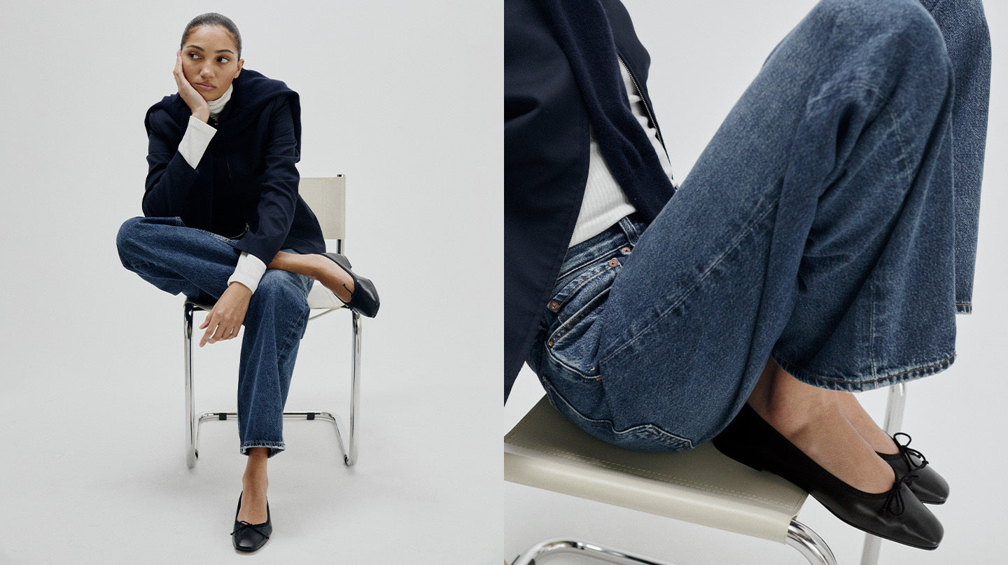 Person sitting on a chair wearing a dark jacket, white shirt, blue jeans, and black shoes.