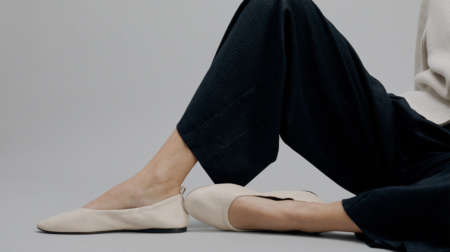 Person wearing beige flats and dark pants on a gray background