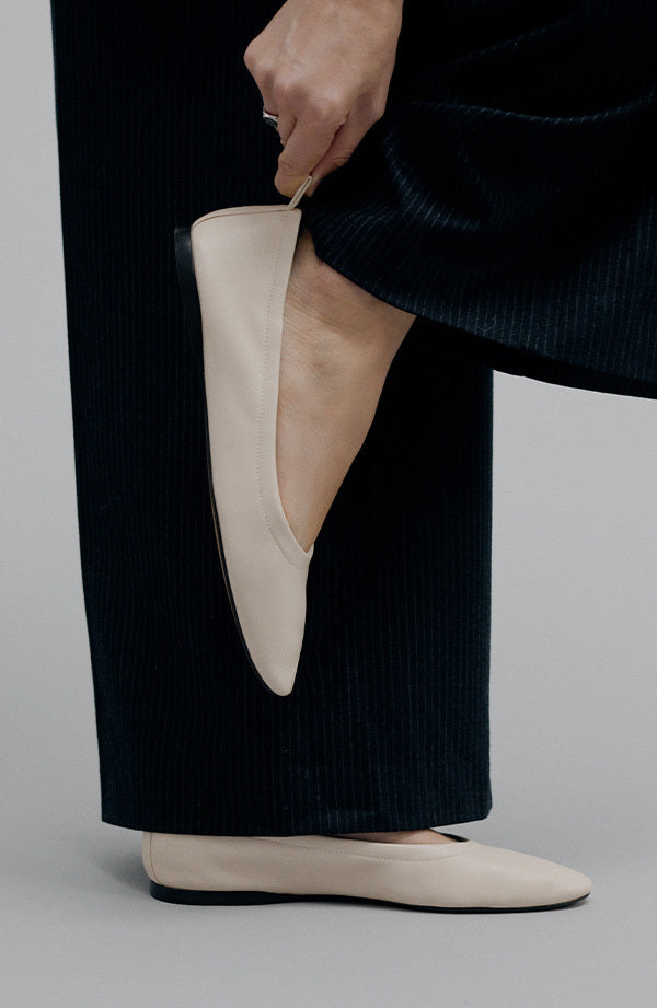 Person wearing beige flat shoes with dark pants on a neutral background