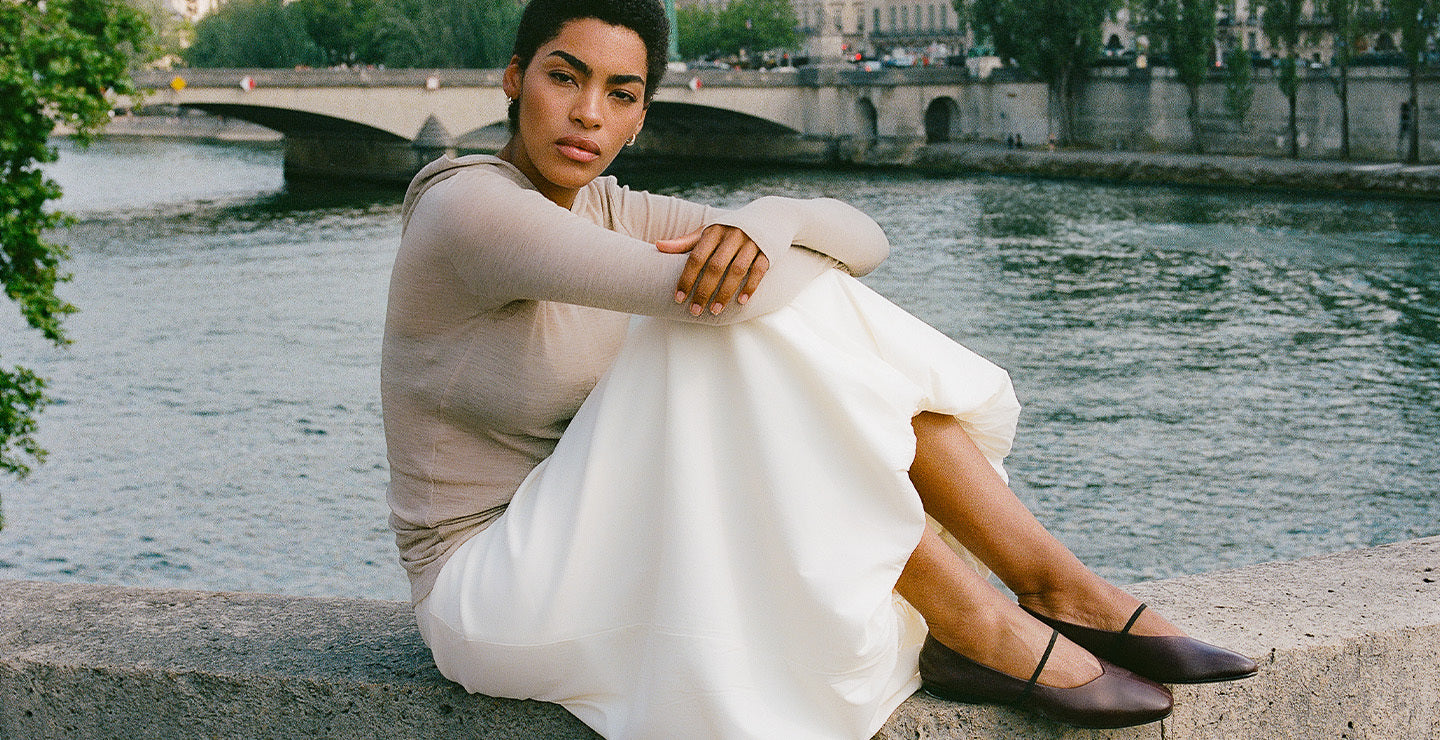 Woman in a white dress sitting by a river with a bridge in the background