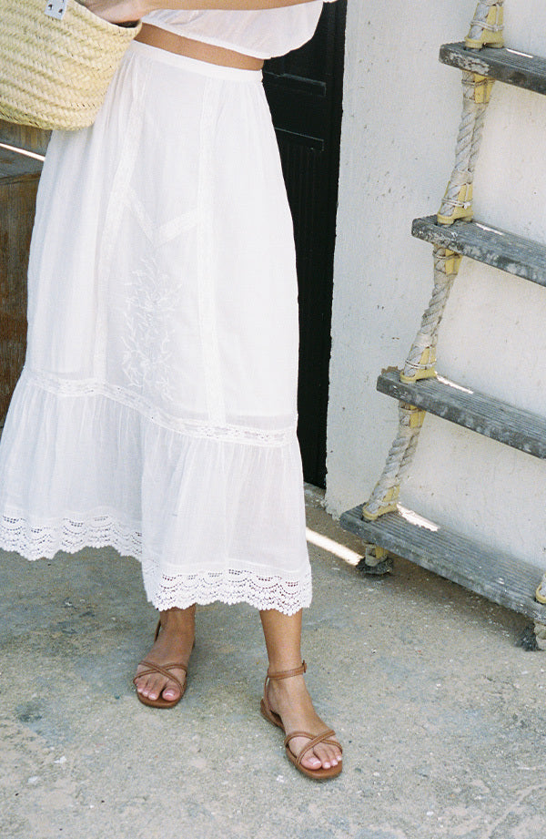 Person wearing a white lace skirt and saddle flat sandals in the summer. 