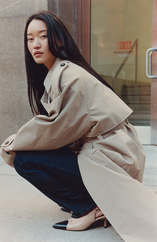 Woman in a beige trench coat squatting on a sidewalk