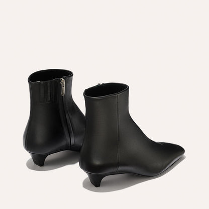 A pair of Alex Mill x Margaux: The Inga - Black Calf ankle boots by margaux-development, crafted in black leather with low kitten heels and side zippers; one boot displays the zipper, the other shows a sleek NYC-inspired silhouette.