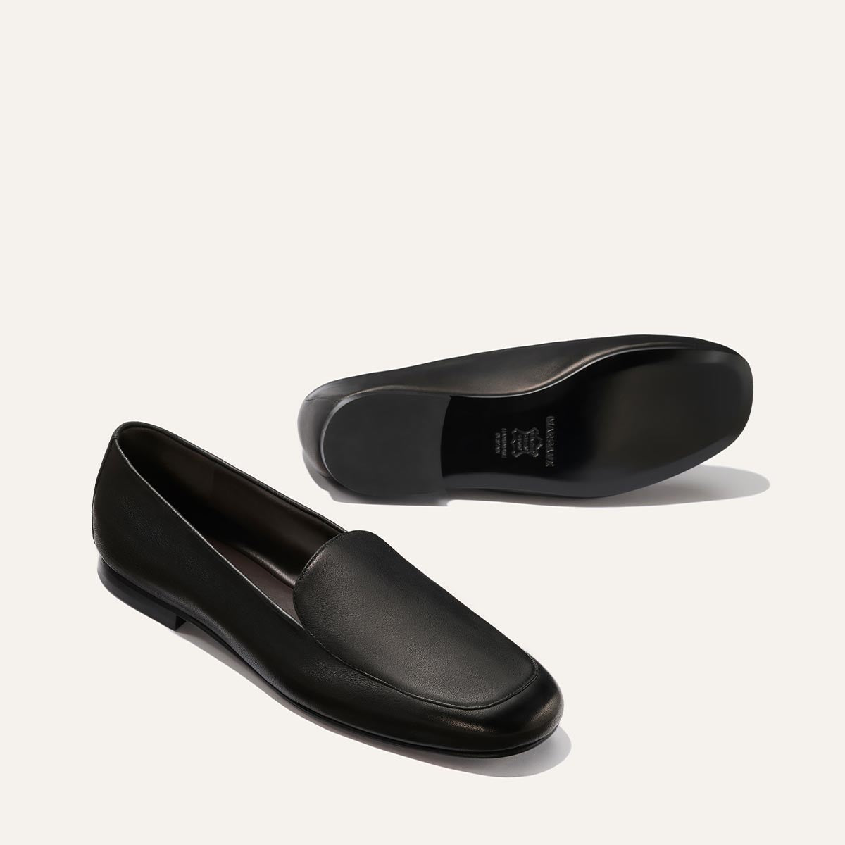 The James Loafer - Black Nappa by Margaux: one black leather loafer stands upright while the other lies on its side to show the sole, both set against a plain light background.