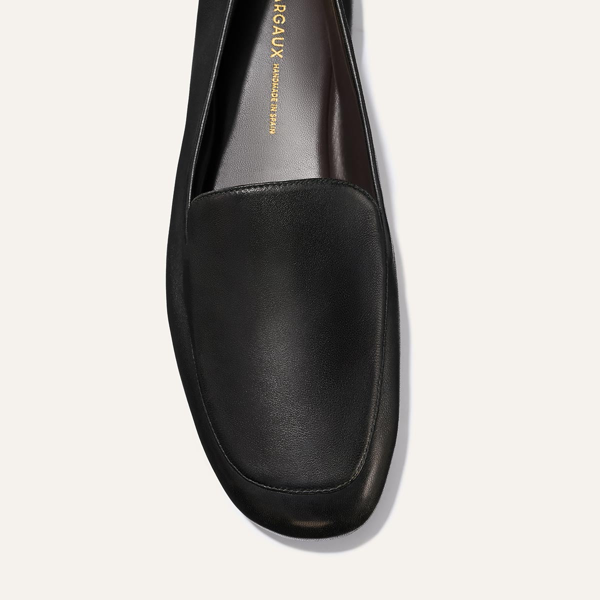 Top view of The James Loafer - Black Nappa by Margaux, a single black leather shoe with a rounded toe and visible insole featuring gold branding.