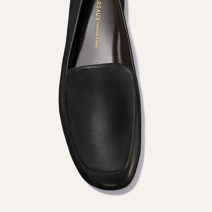 Top view of The James Loafer - Black Nappa by Margaux, a single black leather shoe with a rounded toe and visible insole featuring gold branding.