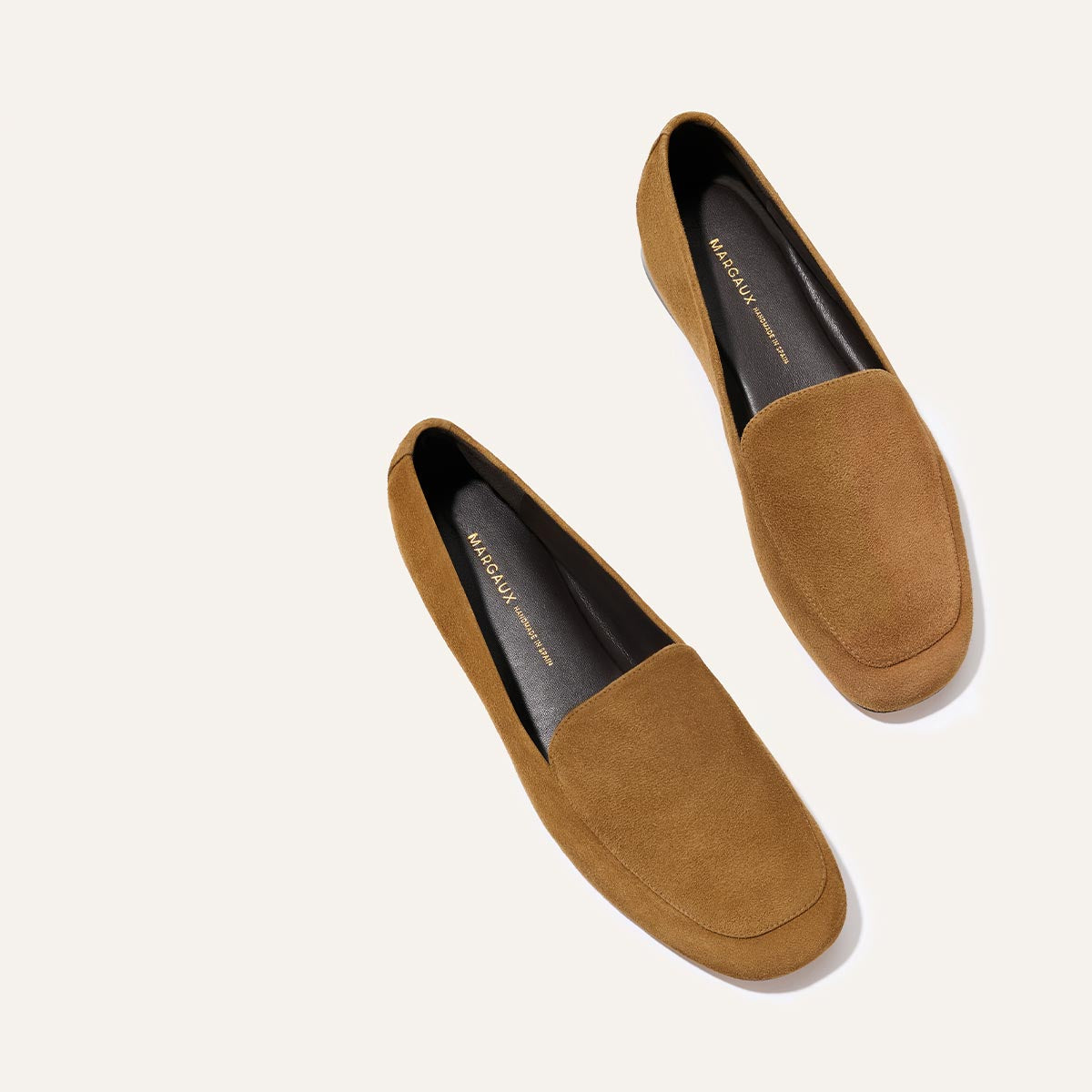 The James Loafer - Cedar Suede by Margaux, featuring brown suede and black insoles, displayed diagonally on a light beige background with the left shoe below and the right above.