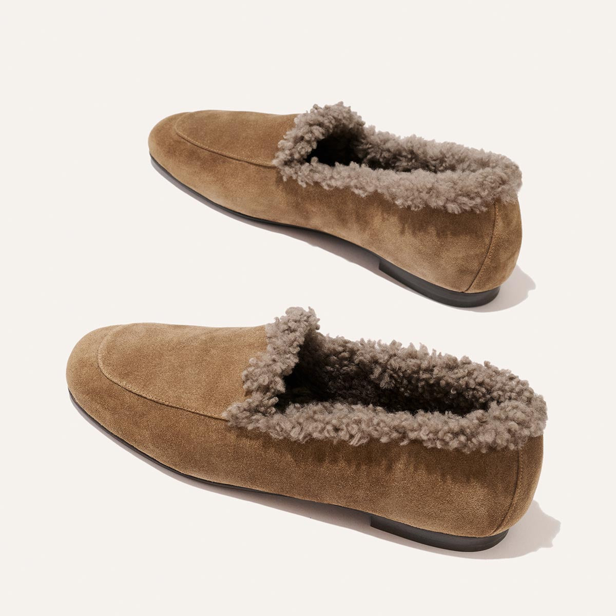 The James Loafer in Driftwood Suede and Shearling, featuring two tan suede loafers with a shearling lining and handcrafted sacchetto construction.