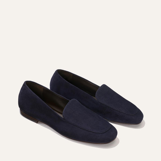 The James Loafer in Indigo Suede by Margaux features a refined, slip-on silhouette and sacchetto construction for a tailored fit, elegantly presented against a light beige background.