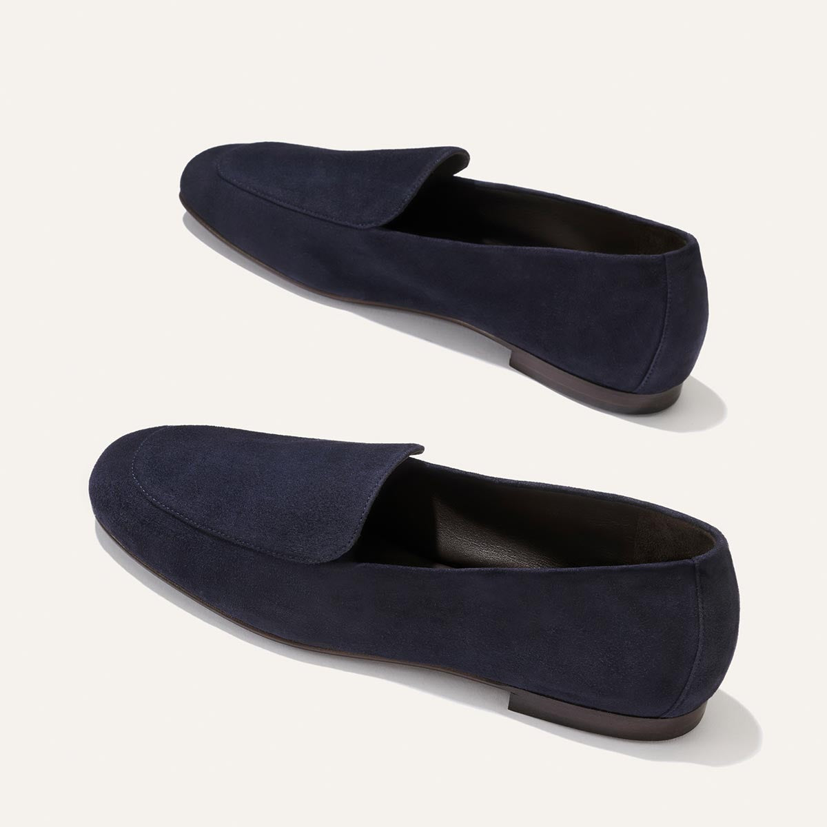 The James Loafer - Indigo Suede by Margaux is showcased on a light background, featuring a minimalist silhouette, low heel, and rounded toe in rich dark blue suede. Expertly handmade with sacchetto construction for outstanding flexibility and comfort, these loafers deliver a tailored fit with each step.