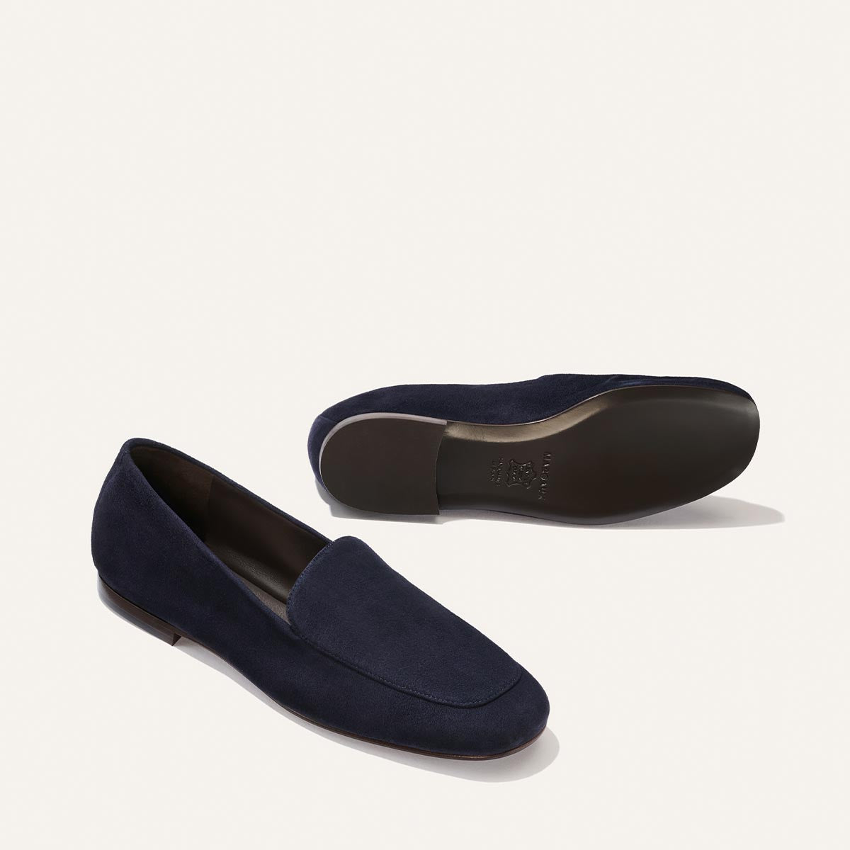 A pair of The James Loafer by Margaux in indigo suede, expertly crafted using sacchetto construction for a tailored fit—one shoe is angled to reveal the top and side, while the other displays the sole, both set against a simple light background.