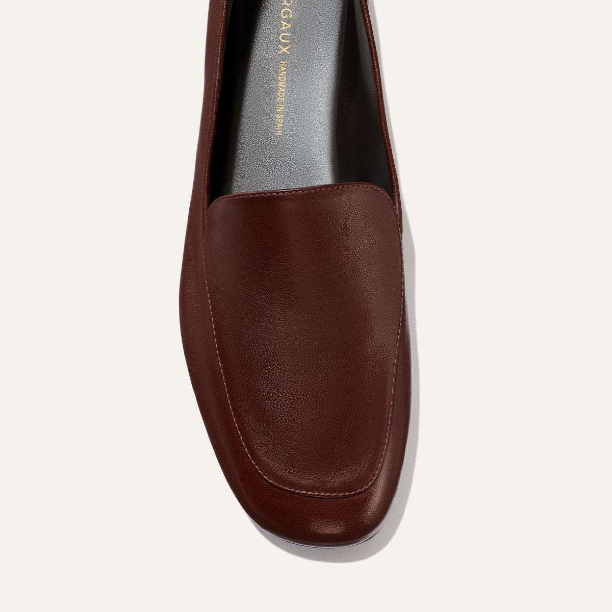 A top view of The James Loafer in Mahogany Nappa by Margaux, a handmade brown leather loafer featuring visible stitching, a smooth rounded toe, and part of the gray insole with gold text—crafted for slipper-level comfort.