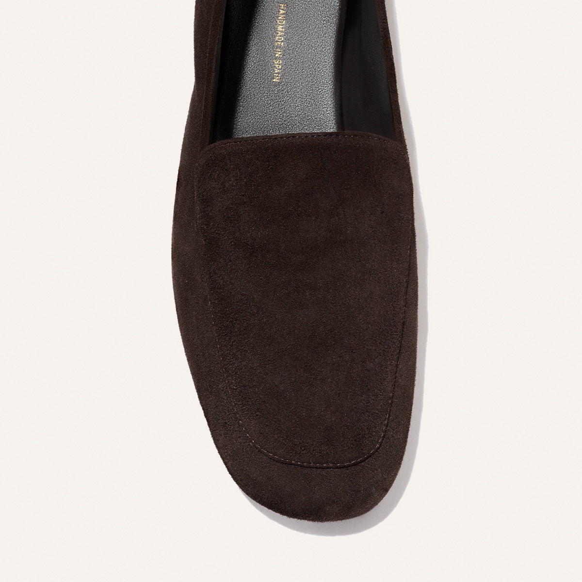 A close-up, top-down view of Margaux’s The James Loafer in Molasses Suede highlights the rich dark brown suede, refined toe shape, and tailored foot opening for a sophisticated fit against a light background.