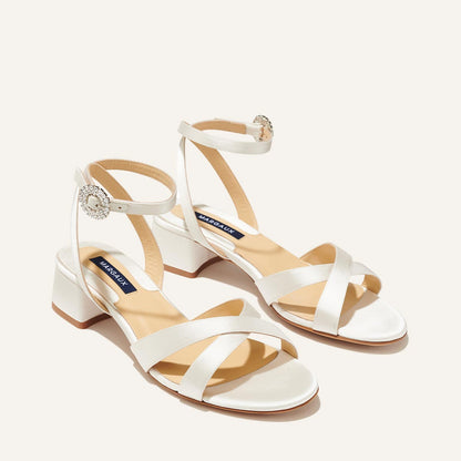 The Lena Sandal in metallic Ivory Satin, featuring perfectly placed straps, a crystal buckle, and a comfortable 1.5-inch block heel.