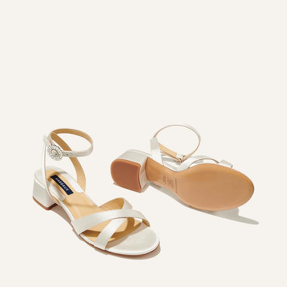The Lena Sandal in metallic Ivory Satin, featuring perfectly placed straps, a crystal buckle, and a comfortable 1.5-inch block heel.