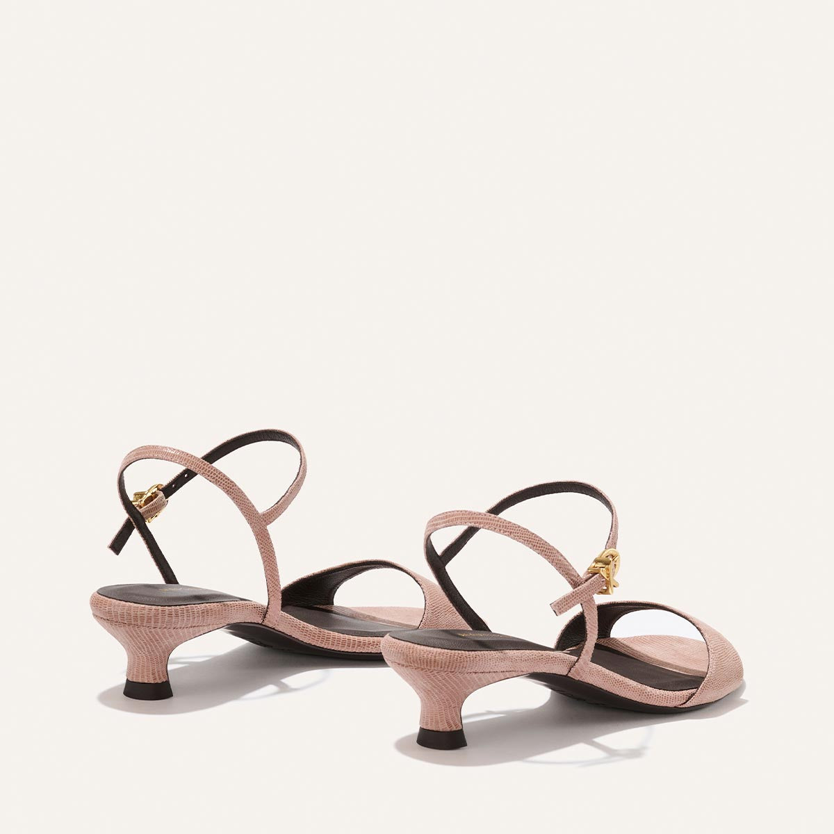 Pair of pink high-heeled sandals with thin straps on a light beige background