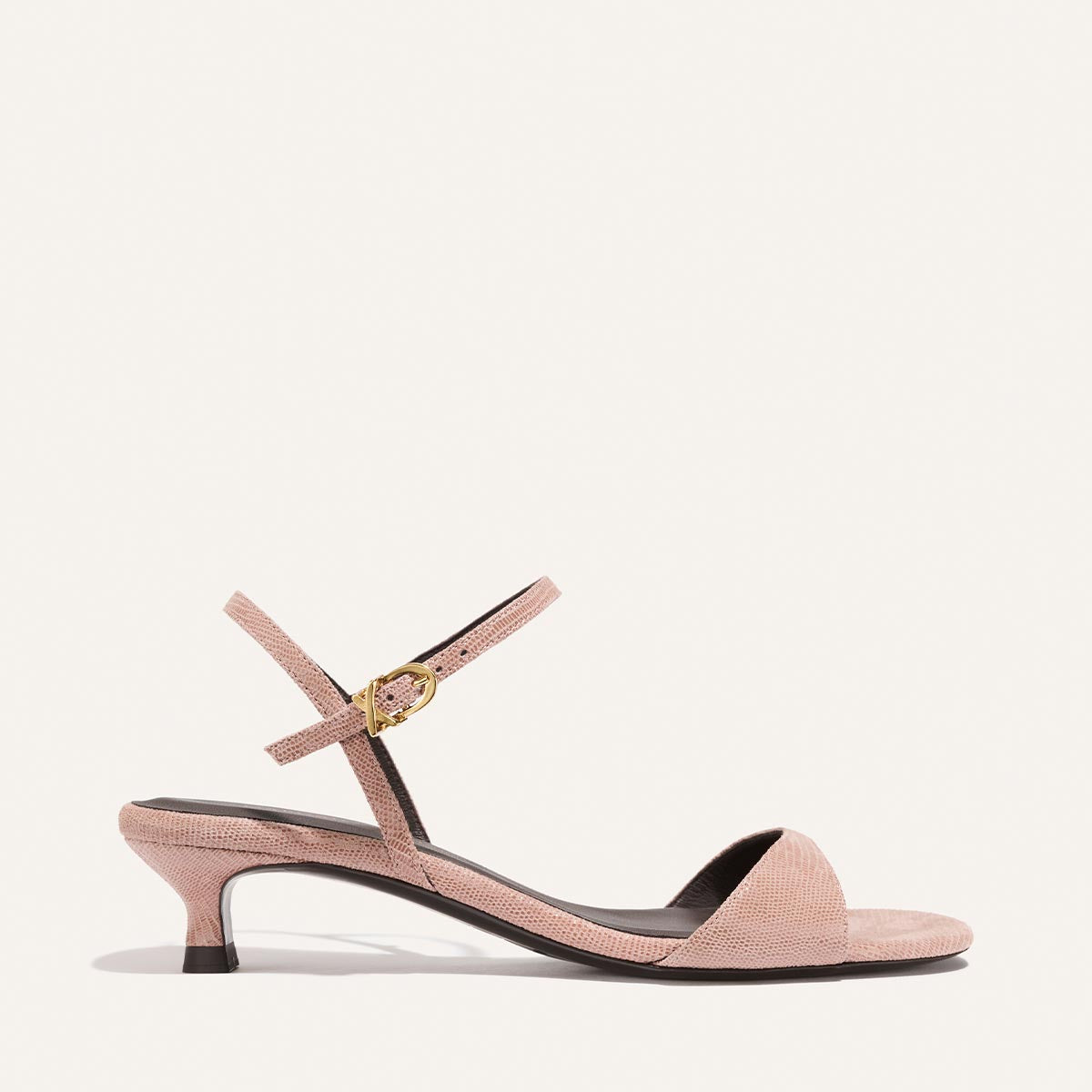 Pink sandal with a thin strap and gold buckle on a white background