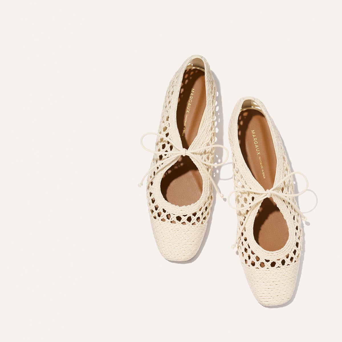 The Luna - Ecru Macrame by Margaux are cream-colored cotton ballet flats with lace-up ties, rounded toes, and intricate cut-outs—ideal for easy summer style. Displayed on a light background.
