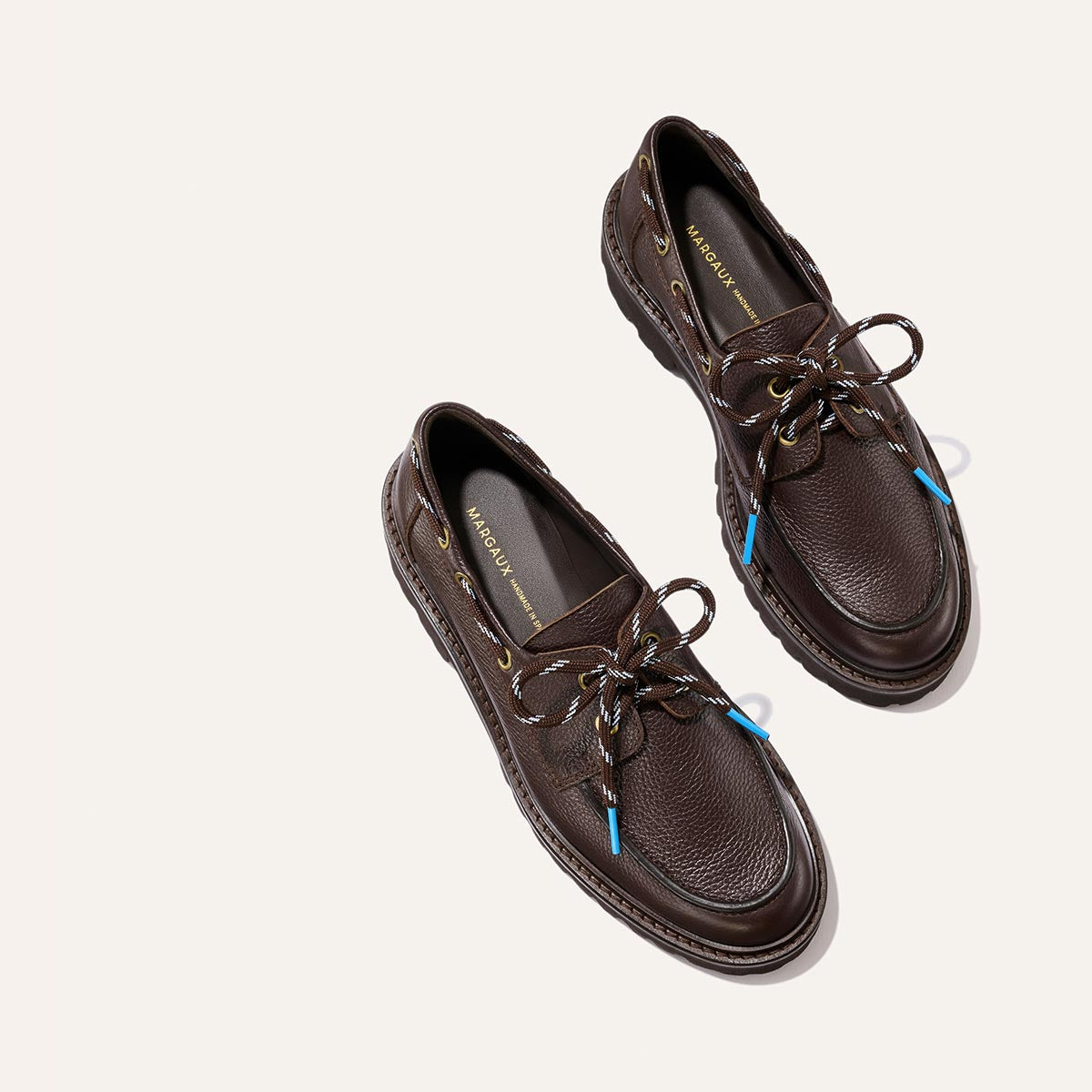 A pair of The Marine Loafer - Espresso Tumbled Calf by Margaux, featuring dark brown textured leather uppers, decorative laces with light blue aglets, displayed side by side on a light background.