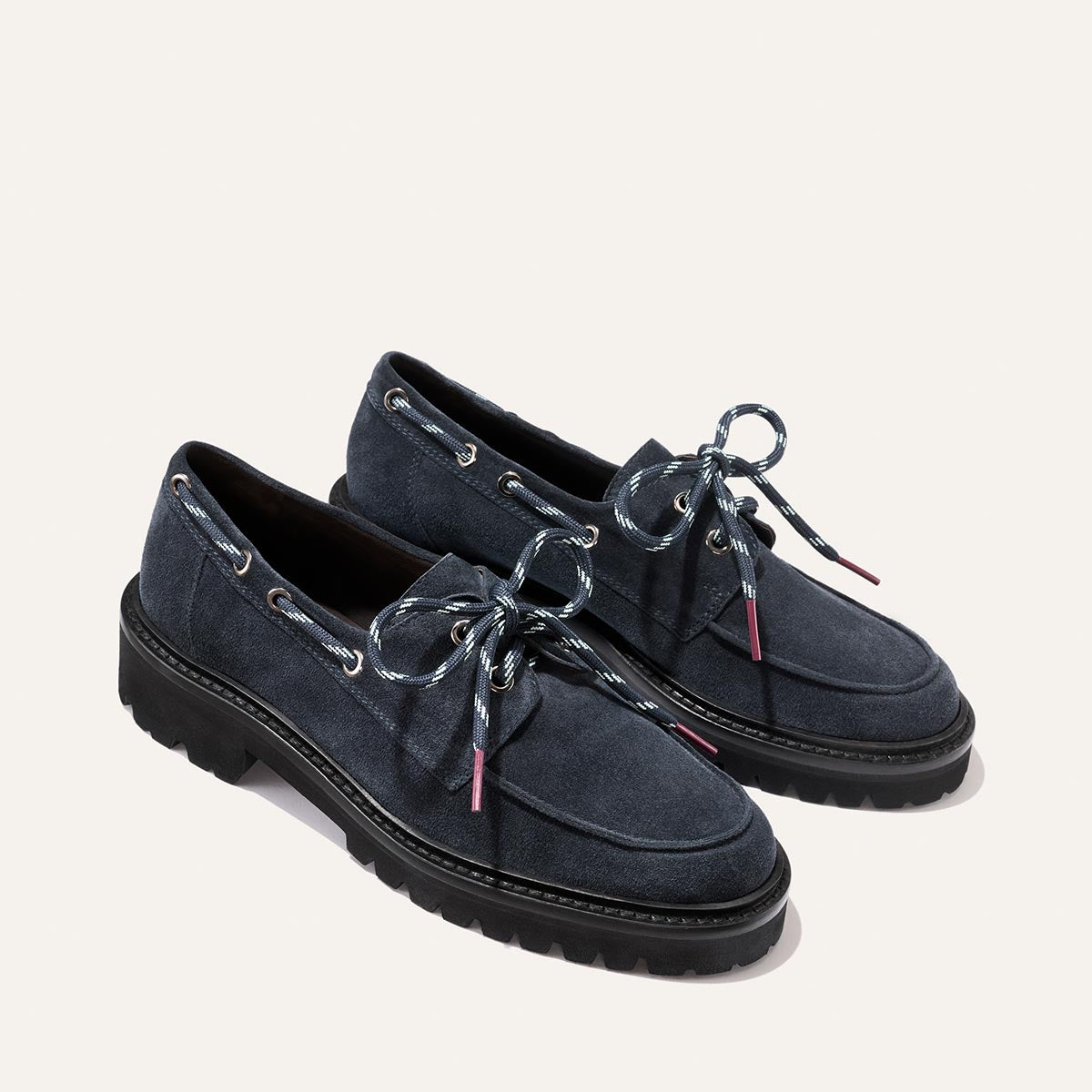 A pair of Margaux’s The Marine Loafer in vintage navy suede, featuring thick black soles, metallic eyelets, and blue-and-white striped bow laces.