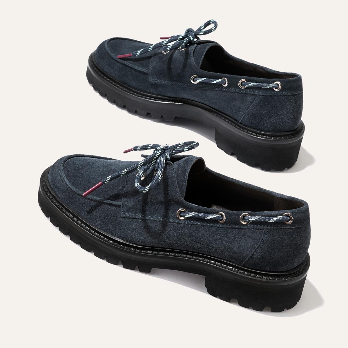 The Marine Loafer in Vintage Navy Suede by Margaux, featuring thick black soles and blue-and-white striped laces, is displayed on a plain light background.