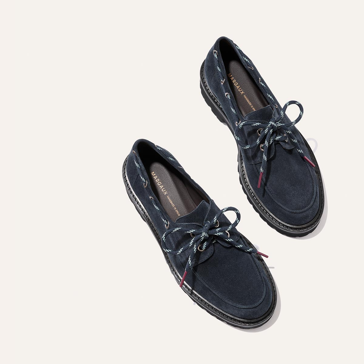 Showcased against an off-white background, The Marine Loafer in Vintage Navy Suede by Margaux features black rubber soles and patterned blue laces.