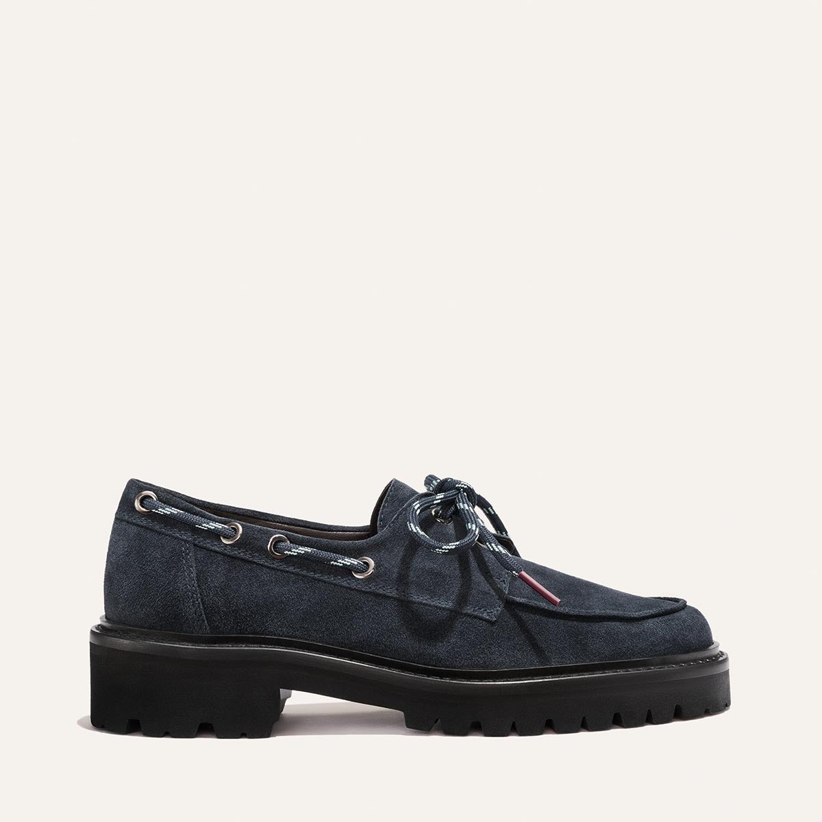 Margaux’s The Marine Loafer in vintage navy suede features silver eyelets, blue-and-white laces, and a chunky black lug sole, shown against a light background.