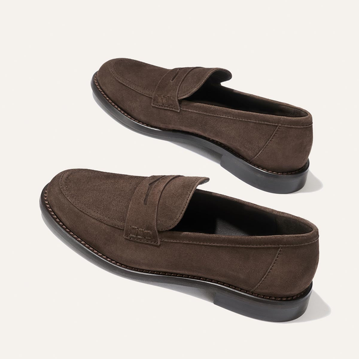 The Marlowe Loafer - Umber Suede by Margaux, shown on a light background, features a modern take on the classic penny loafer design with visible stitching and black soles—making it a versatile closet staple.