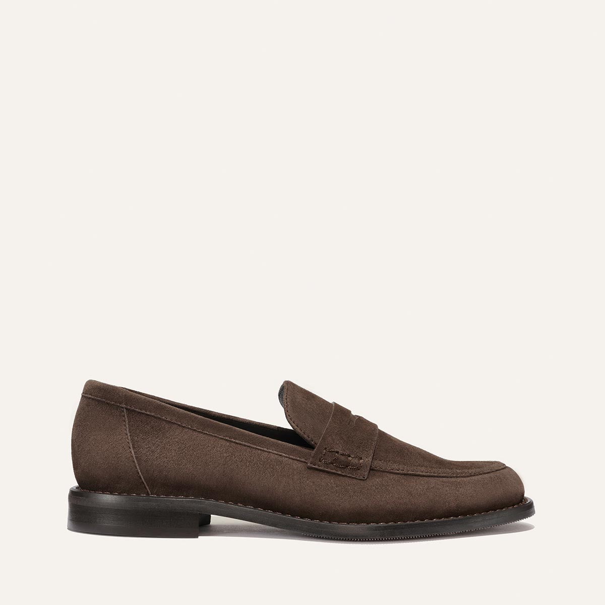 The Marlowe Loafer - Umber Suede by Margaux is a timeless closet staple, featuring a brown suede finish, classic penny strap, and low black heel. Shown in side profile against a plain off-white background, this modern loafer embodies effortless style.