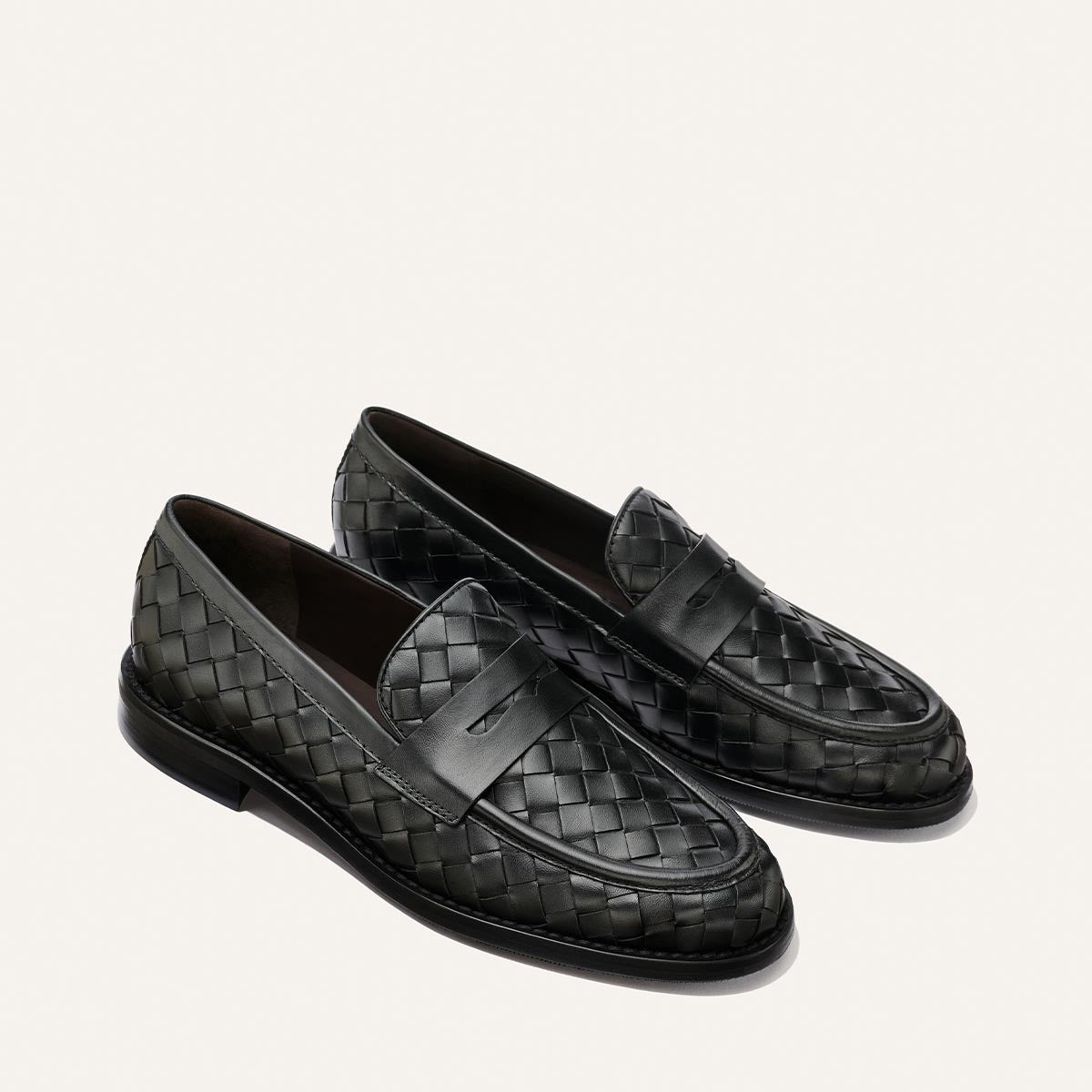 A pair of The Marlowe Loafer in Black Woven Pasado Calf by Margaux, featuring a classic penny strap and sleek leather weaving, shown at a slight angle on a plain white background—these modern loafers are a true closet staple.