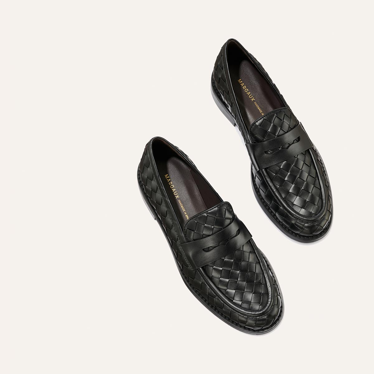 A pair of Margaux’s The Marlowe Loafer in Black Woven Pasado Calf, featuring woven leather and a smooth band detail across the top, photographed on a light background.