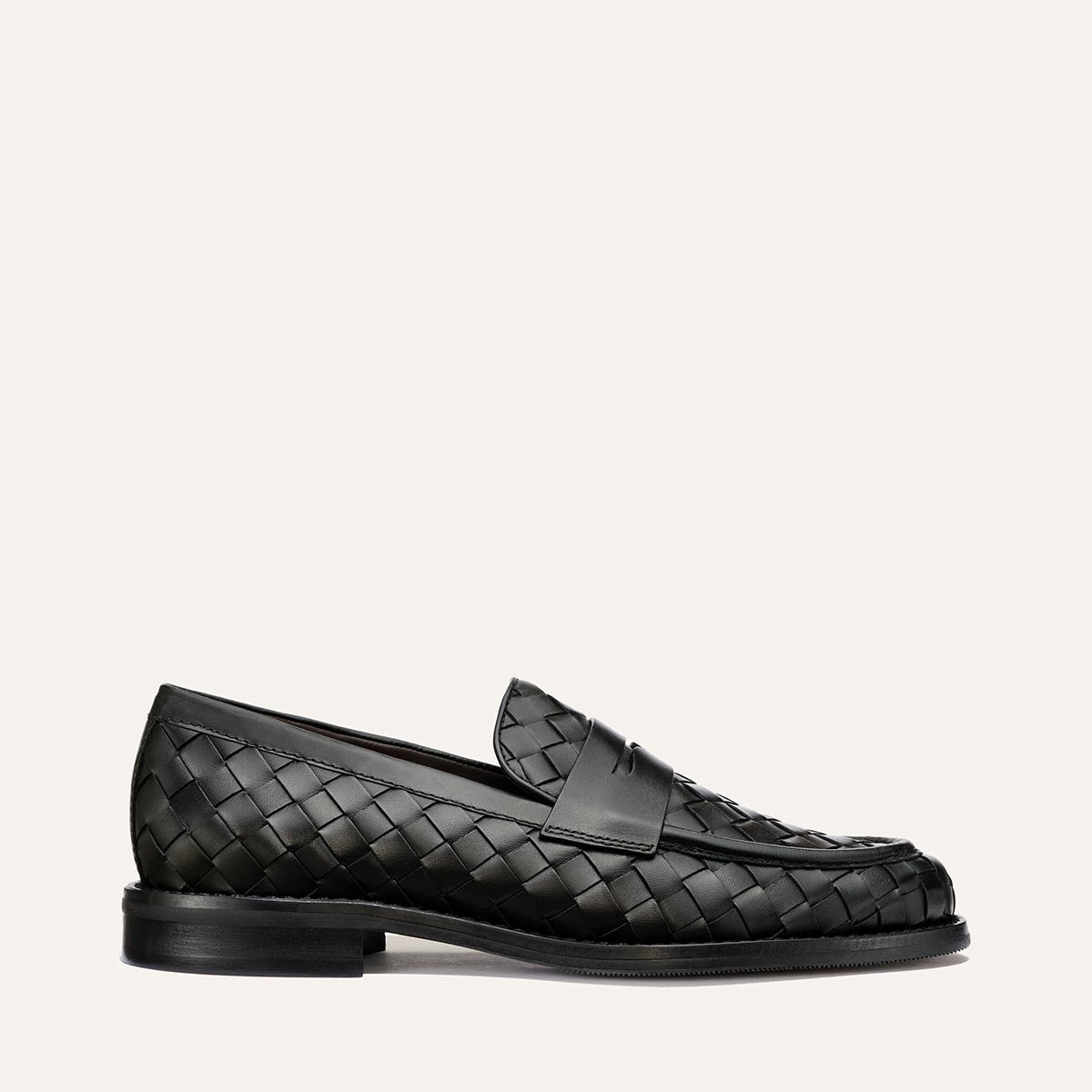 The Marlowe Loafer by Margaux in Black Woven Pasado Calf features a low heel and rounded toe, shown in profile on a simple light background—a modern loafer designed to be a closet staple.