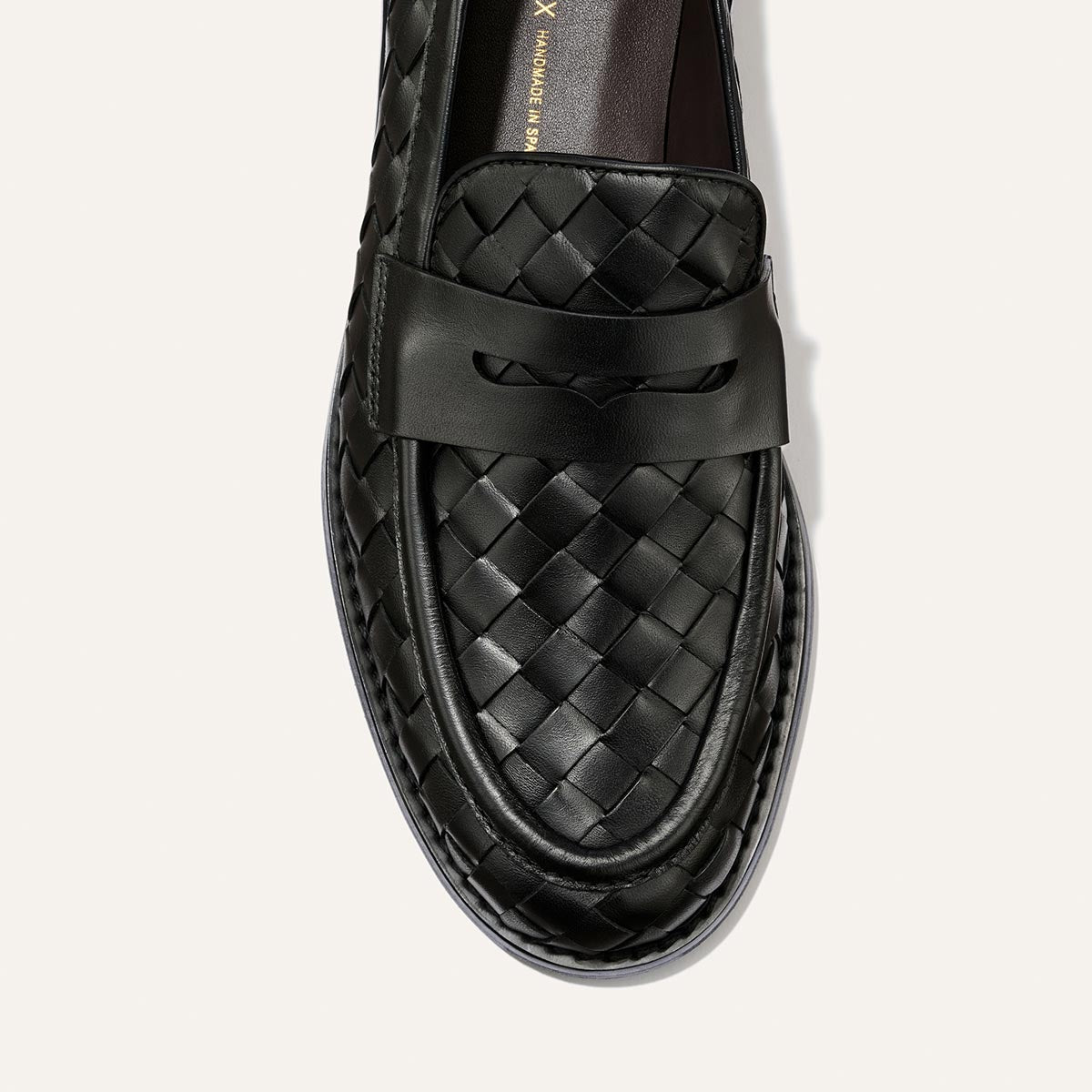 A close-up of Margaux’s The Marlowe Loafer in Black Woven Pasado Calf, featuring a solid leather strap across the upper and photographed from above on a light background—a true closet staple for those seeking modern loafers with timeless appeal.