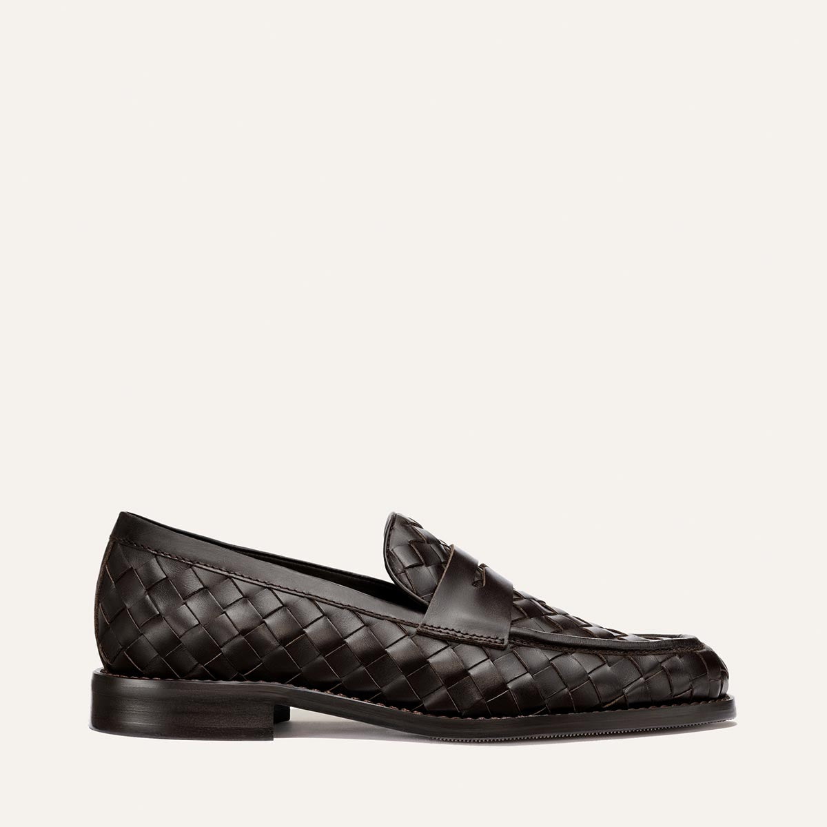The Marlowe Loafer by Margaux in Brown Woven Pasado Calf features a dark brown woven leather design, a low heel, and a smooth sole. Shown in profile against an off-white background, it’s an effortlessly modern staple for any wardrobe.