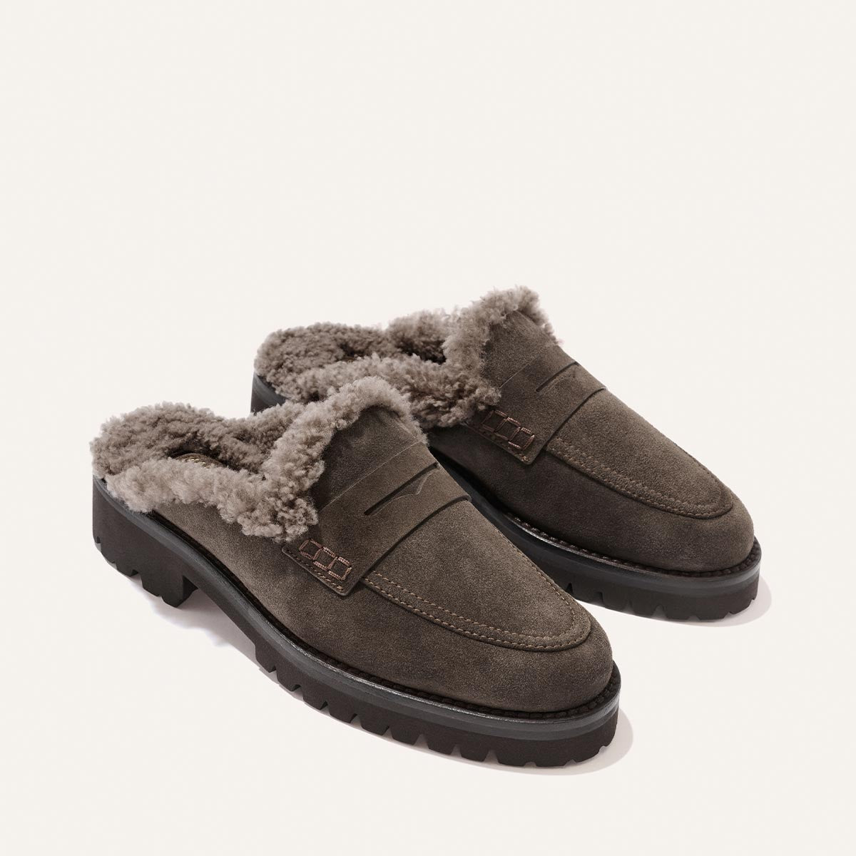 The Marlowe Mule by Margaux in English Brown Suede and Shearling is a pair of cozy slide loafers featuring thick shearling lining and black rubber soles, shown against a white background.