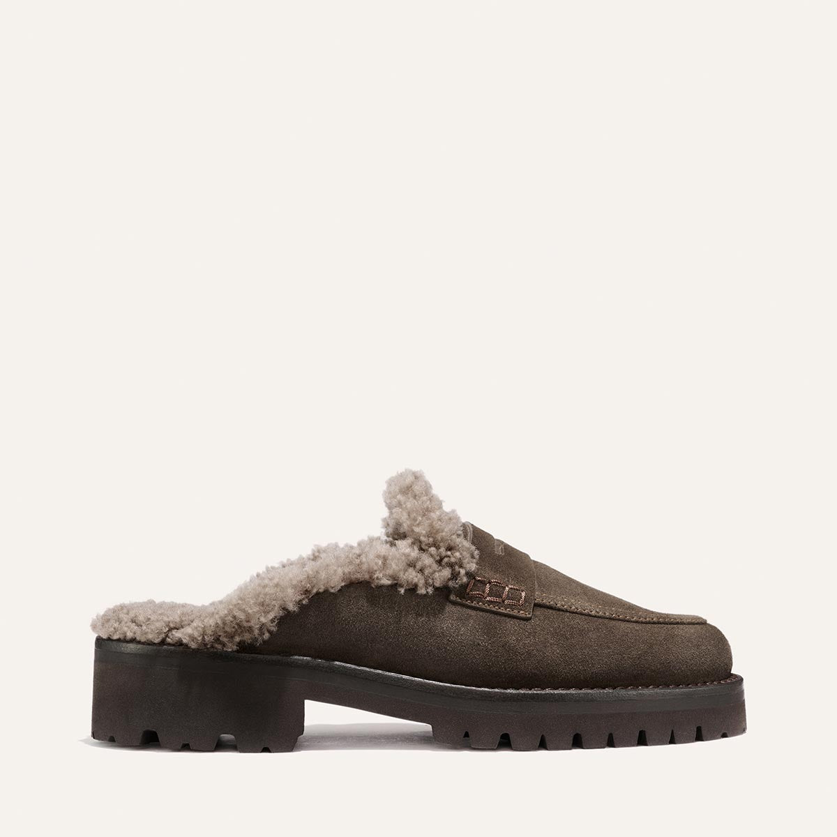 The Marlowe Mule by Margaux features plush beige shearling lining and a chunky rubber sole, crafted in cozy English brown suede. Displayed in profile against a plain white background.