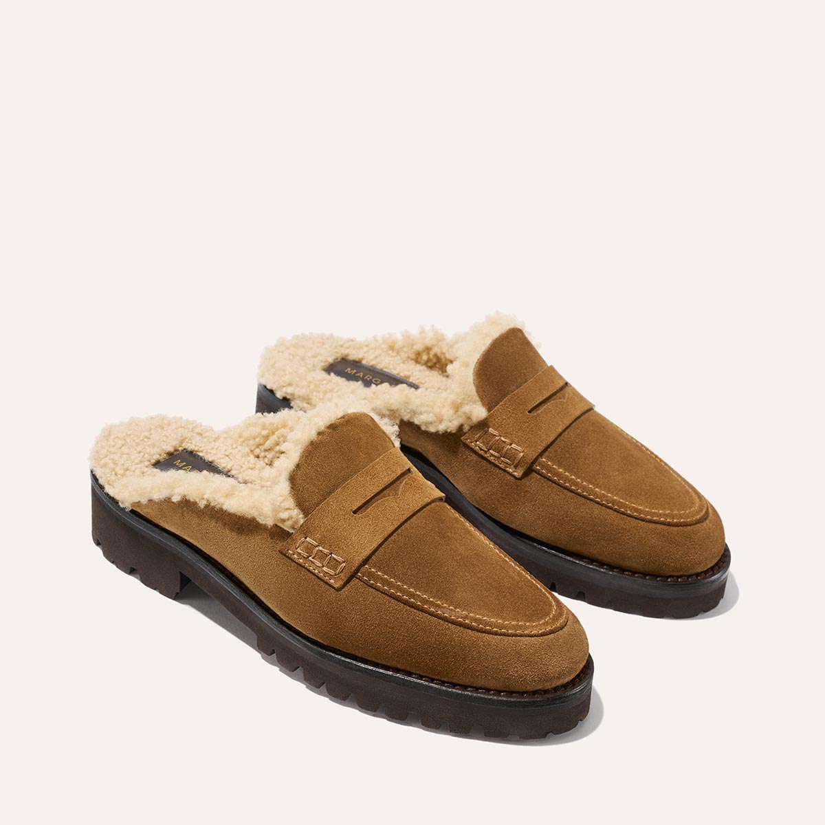 Margaux's The Marlowe Mule in walnut suede features cozy cream shearling lining and black rubber soles, shown on a light background.
