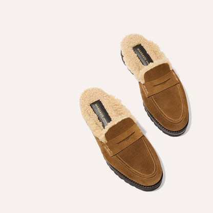 Margaux’s The Marlowe Mule in walnut suede features beige shearling lining, black soles, and visible brand labels on the insoles. The pair is displayed on a light background.
