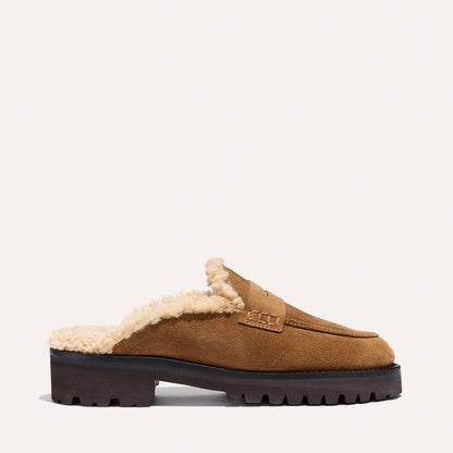 The Marlowe Mule by Margaux features walnut suede, cream shearling lining, and a chunky black sole, shown in profile against a plain light background.