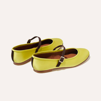 Margaux’s The Demi Jane - Citron Satin features yellow Mary Jane–inspired ballet flats with brown thin straps and small buckles, showcased on a light beige background.