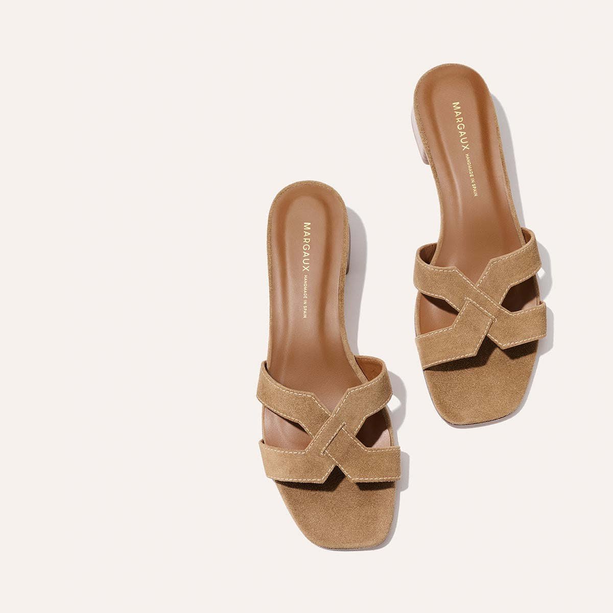 A pair of Margaux’s The MX 35 - Biscotti Suede slide sandals with tan suede crisscross straps and low heels, displayed on a light background.