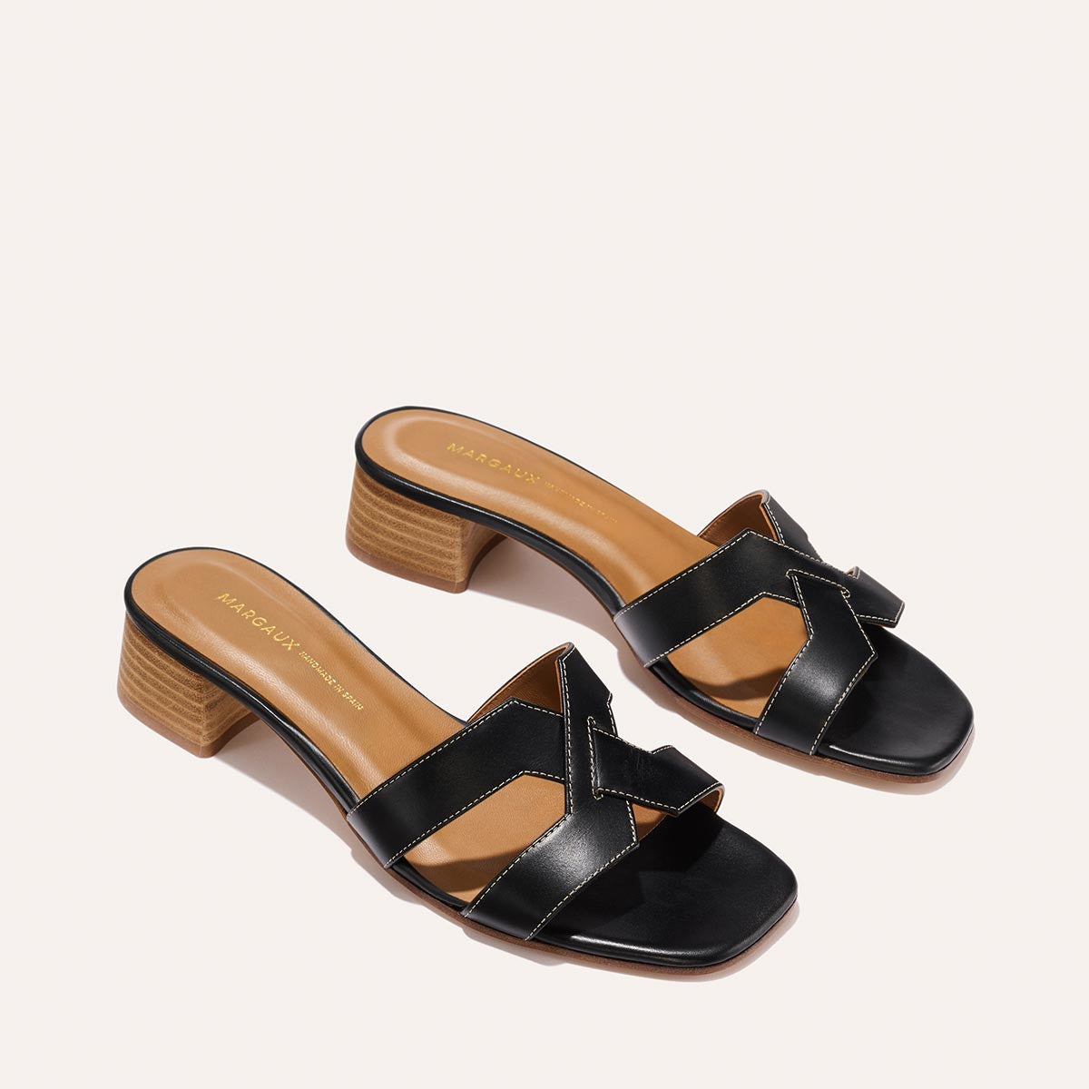 The MX 35 - Black Calf by Margaux-development: black leather slides with criss-cross straps, square toes, and low tan block heels, shown on a light background.